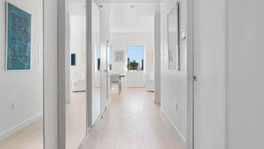 Un couloir moderne avec un parquet en bois clair, des murs blancs et des portes en verre donnant accès aux pièces.