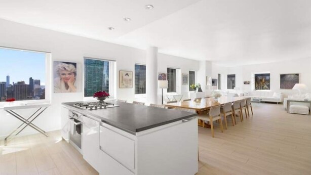 Une cuisine moderne et spacieuse avec un îlot central, un coin repas doté d’une grande table, et un salon avec un canapé et des fauteuils.