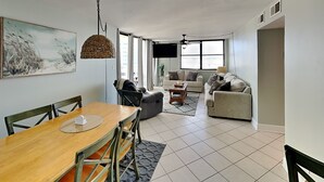Un salon moderne comprenant un coin repas, de grandes fenêtres et un téléviseur à écran plat.