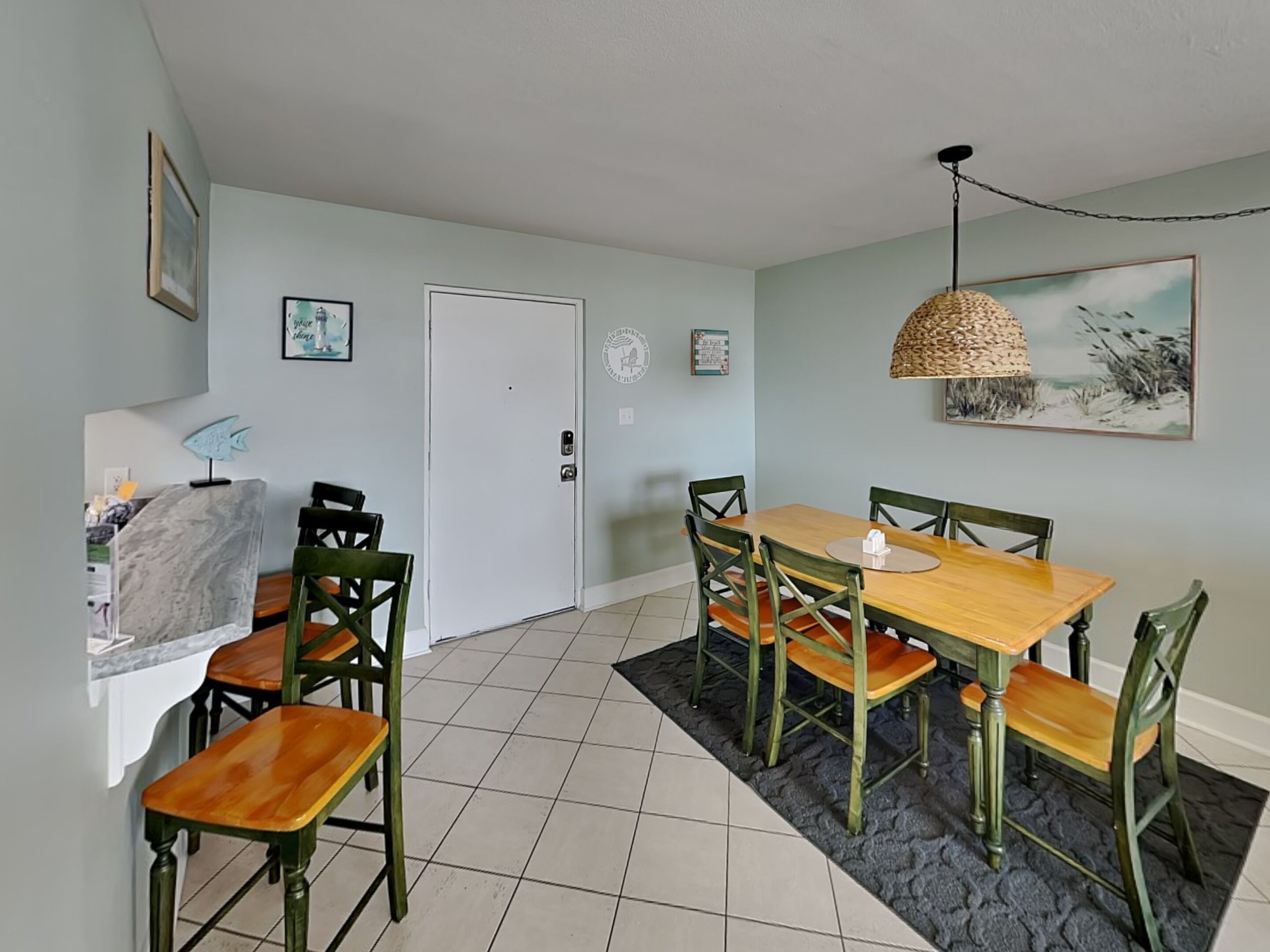 A dining area with a wooden table and chairs, a black textured rug, and a hanging lamp.