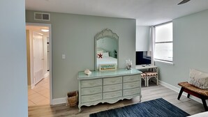 Une chambre à coucher comprenant un lit, une commode, un miroir et un bureau avec une chaise.