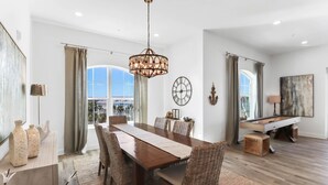 A spacious dining area with a long wooden table, wicker chairs, and a chandelier. - Gulf Place Residences #307 by Southern Vacation Rentals (Santa Rosa Beach)