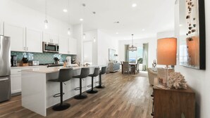 A modern kitchen with white cabinets, a central island with bar stools, and a dining area with a chandelier. - Gulf Place Residences #307 by Southern Vacation Rentals (Santa Rosa Beach)