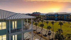 A multi-story building with a balcony, surrounded by palm trees and a parking lot, overlooking a scenic sunset. - Gulf Place Residences #307 by Southern Vacation Rentals (Santa Rosa Beach)