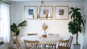 A dining area with a round table, wooden chairs, and framed artwork on the wall. - 3BR/2BA Chic and Tranquil Magnolia House Near Boston (Everett)