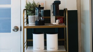 A coffee station with a framed illustration above, a coffee maker, and two coffee containers labeled "Airscape." - 3BR/2BA Chic and Tranquil Magnolia House Near Boston (Everett)