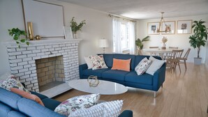 A living room with a blue sofa, a white coffee table, and a brick fireplace. - 3BR/2BA Chic and Tranquil Magnolia House Near Boston (Everett)