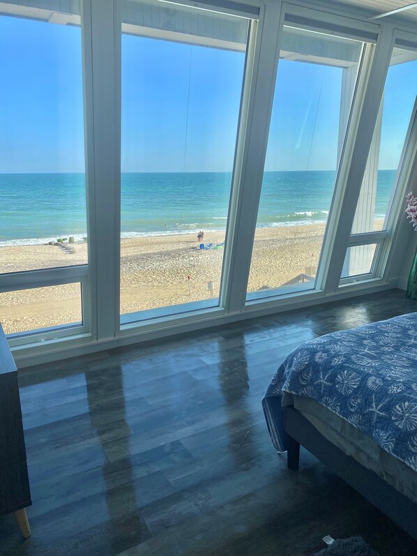 A bedroom with a large window overlooking a beach.
