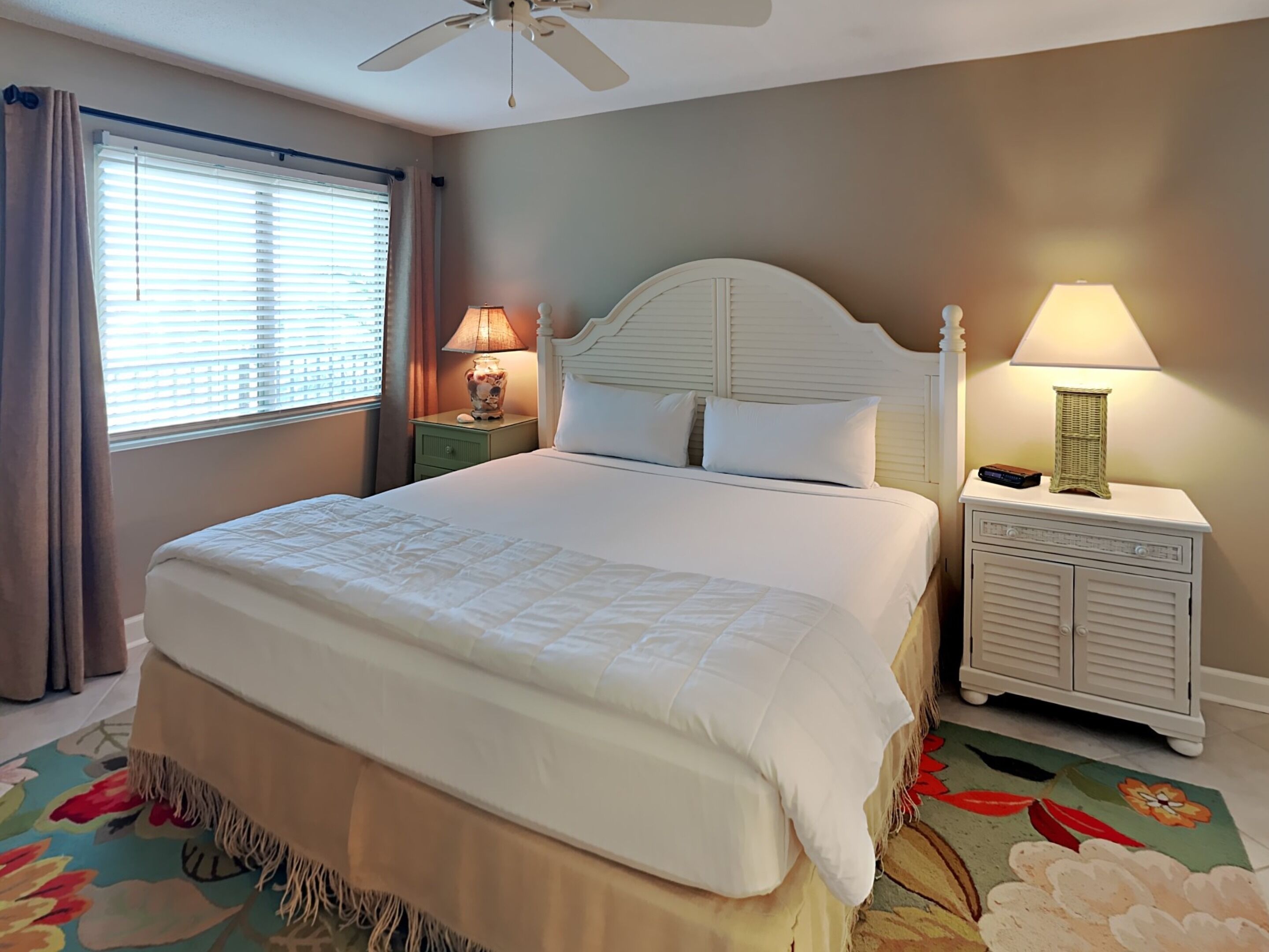 A neatly made bed with a headboard, a nightstand with a lamp, and a window with blinds.