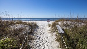 Un sentier de sable qui longe la plage et mène à l’océan, avec un panneau indiquant qu’il n’y a pas de sauveteur en service.