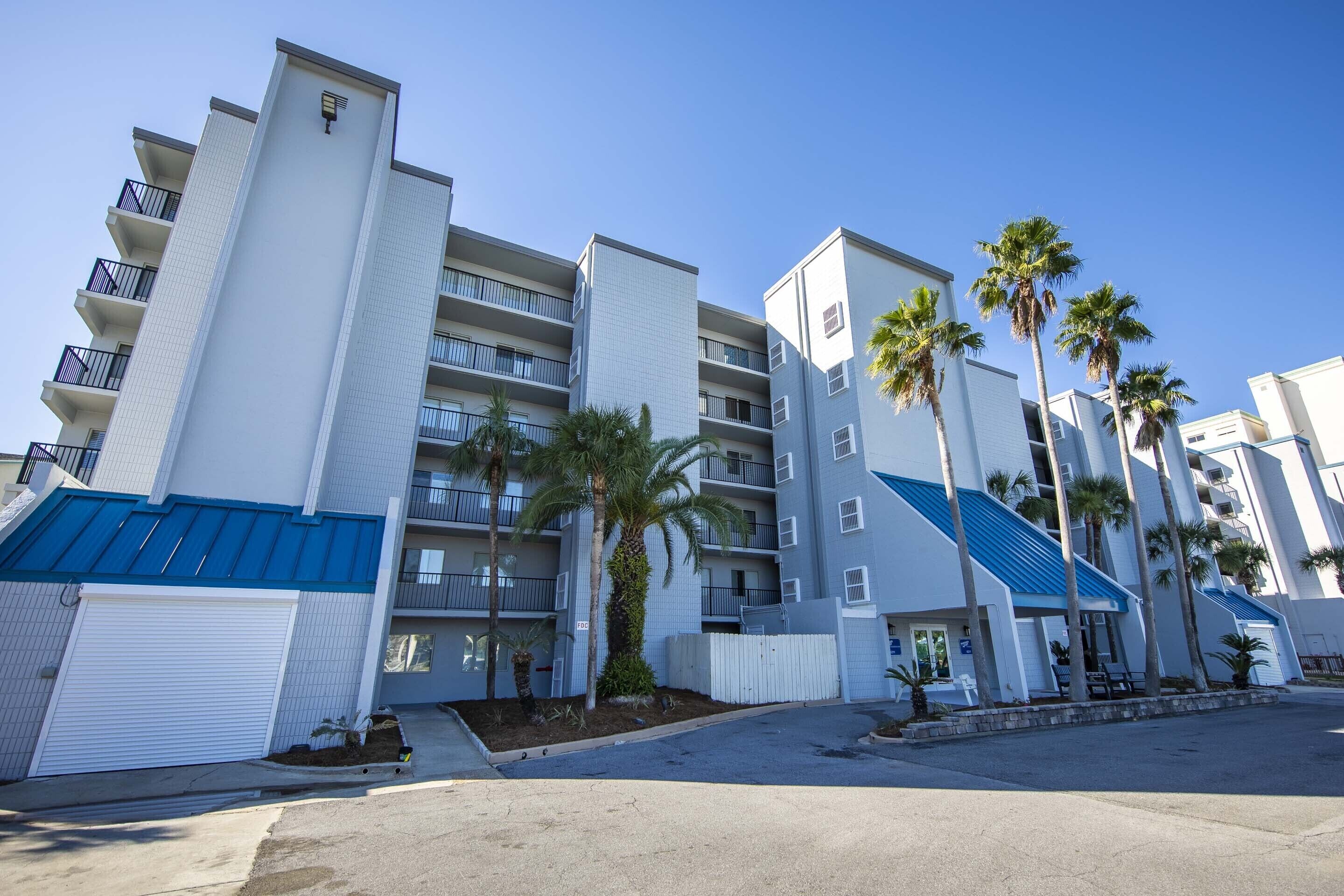A multi-story hotel with balconies, palm trees, and a blue roof.