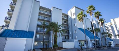 A multi-story hotel with balconies, palm trees, and a blue roof.
