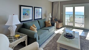 Un salon comprenant un canapé, des fauteuils, une table basse et un balcon avec vue sur la mer.