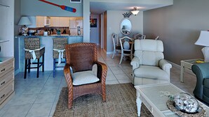 Un salon avec un fauteuil en osier, un canapé blanc et une table basse agrémentée d’objets décoratifs.