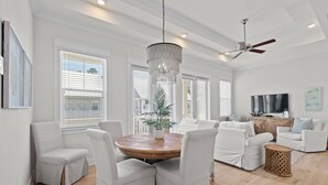 Un salon spacieux avec une table ronde en bois, des chaises à revêtement blanc, un grand lustre et un ventilateur de plafond.