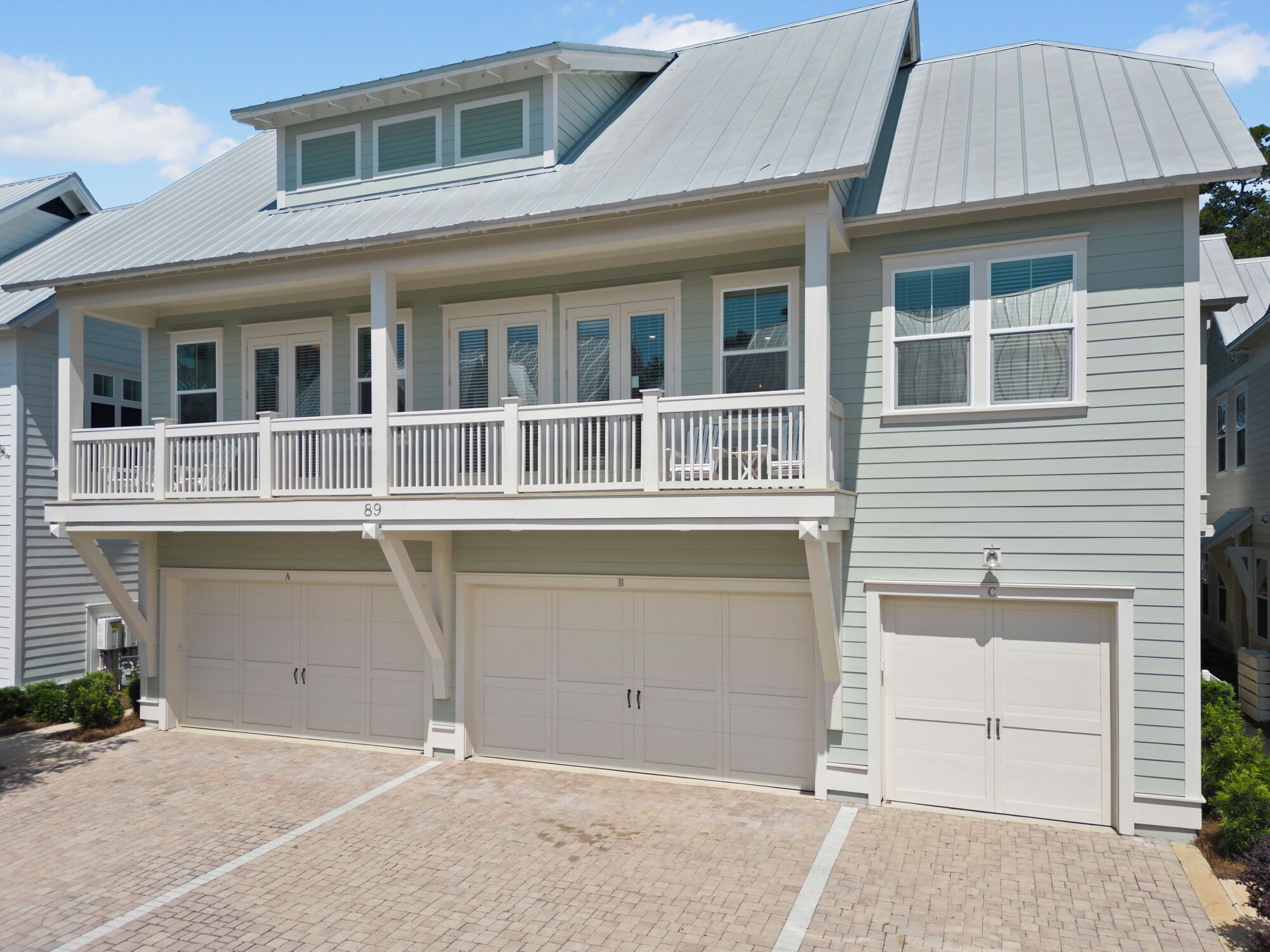 A two-story house with a balcony, two garages, and a brick driveway.