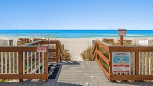 Une promenade en bois menant à une plage, avec un panneau d’avertissement et un panneau indiquant la présence de courants dangereux.