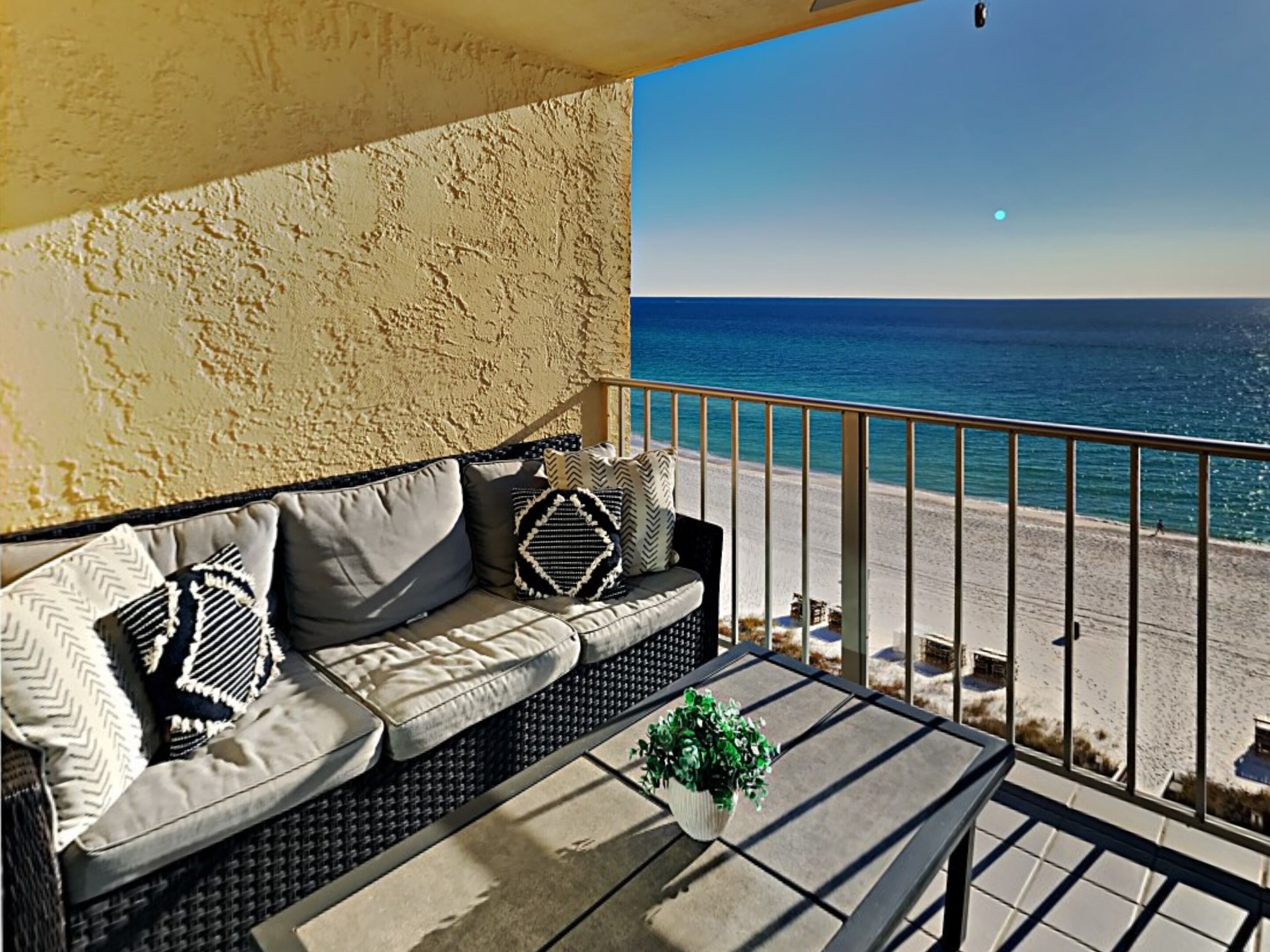 A balcony with a sofa and a table, overlooking a beach.