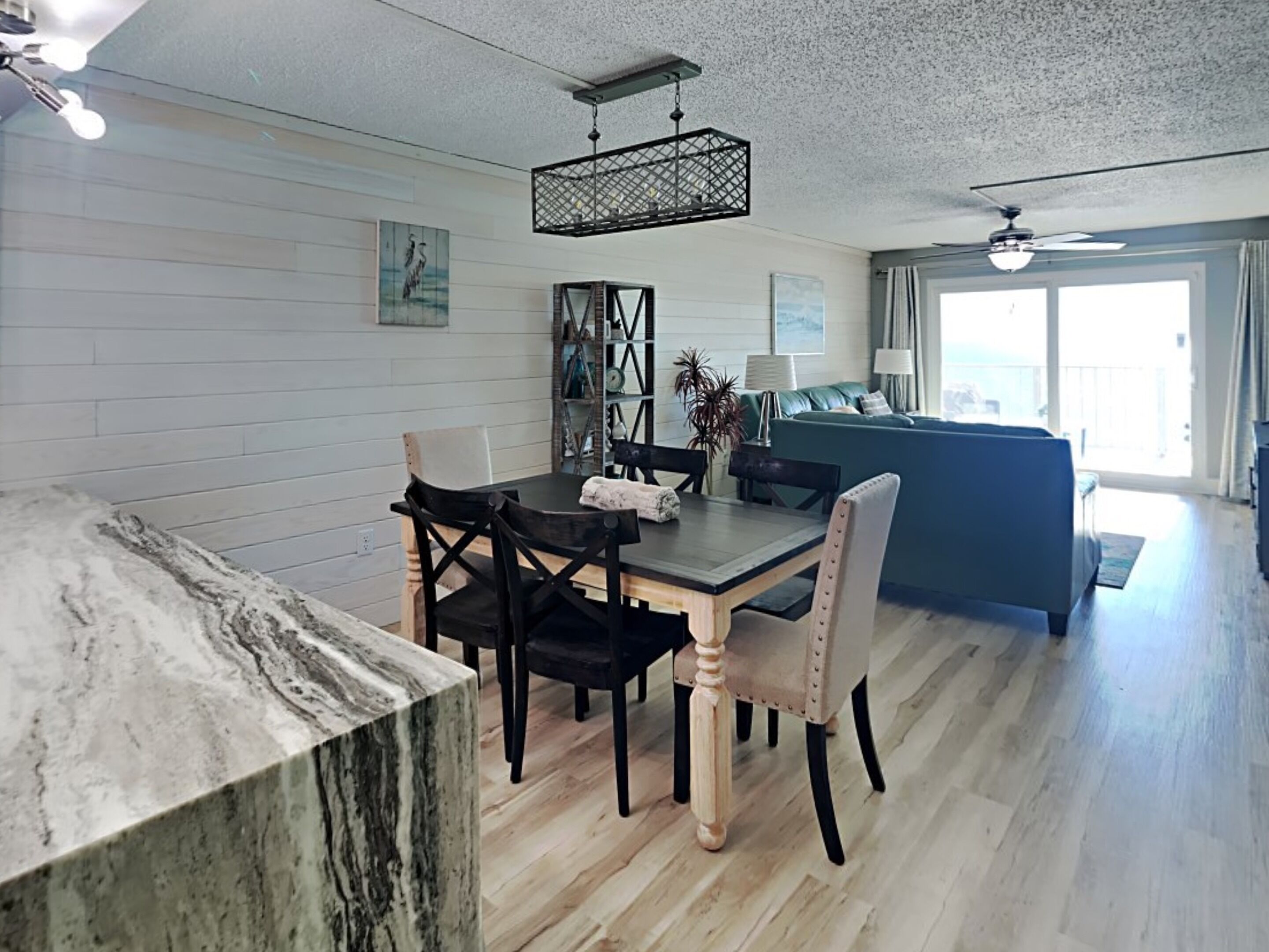 A dining area with a marble table, wooden chairs, and a hanging light fixture.