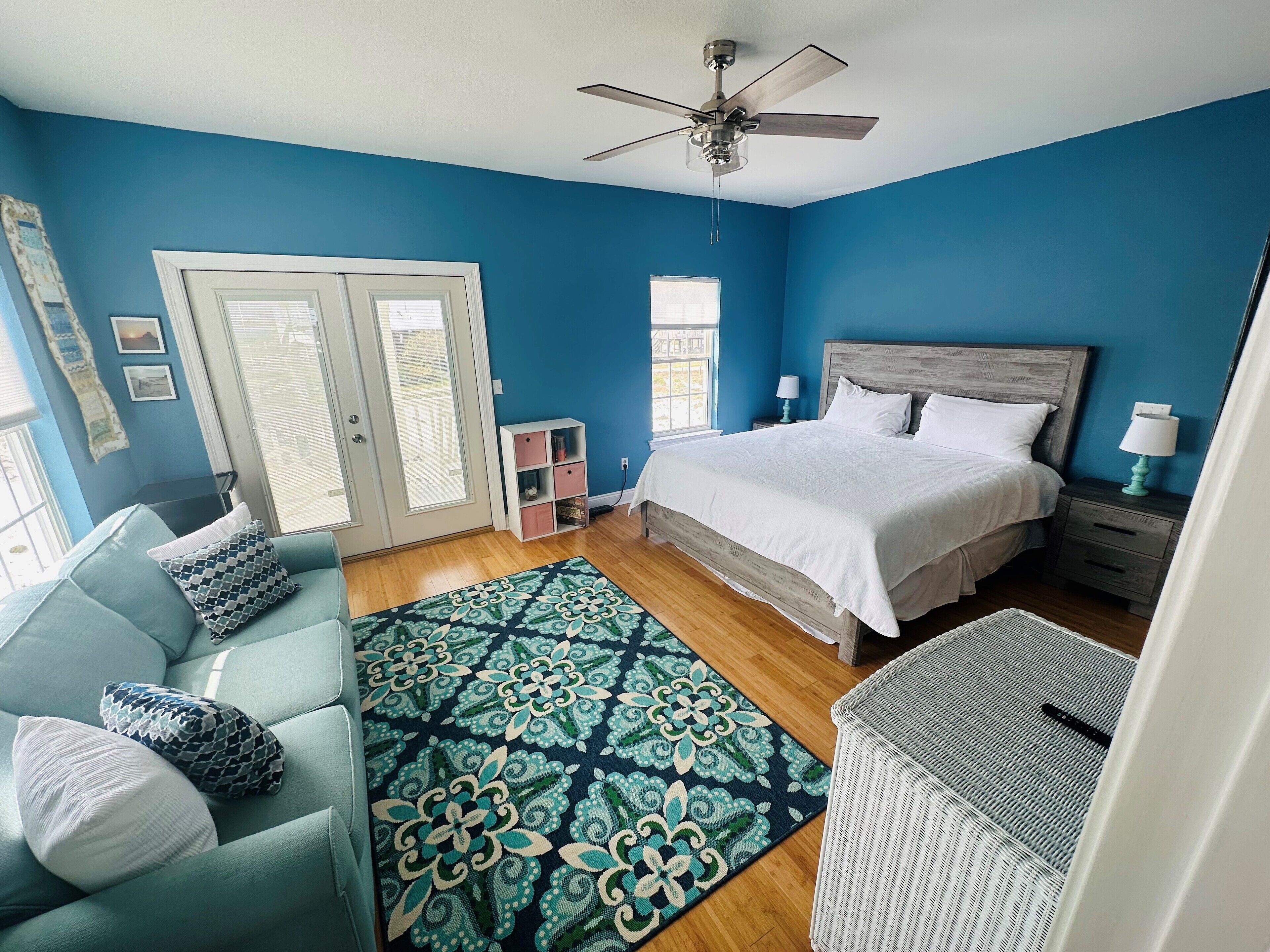 A bedroom with a bed, nightstands, a ceiling fan, a window, and a door.