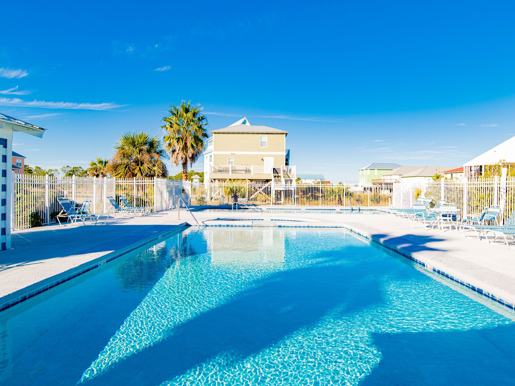A swimming pool with clear blue water, surrounded by white fences and palm trees.