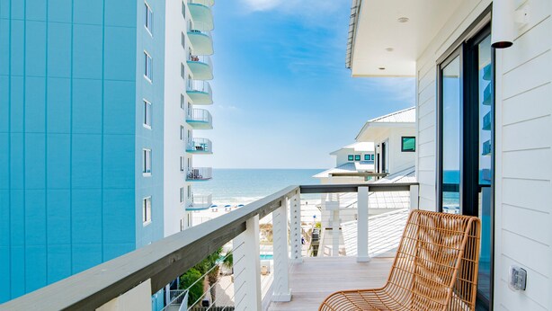A balcony with wicker chairs overlooking a beach and a high-rise building. - The Bluffs at Orange Beach #8 by Southern Vacation Rentals (Orange Beach)