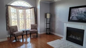 A living room with a fireplace, two armchairs, a round table, and a floor lamp. - Baycation home with Hottub (Lewisporte)