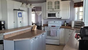 A kitchen with white cabinets, a stove, a microwave, and a coffee maker. - Baycation home with Hottub (Lewisporte)