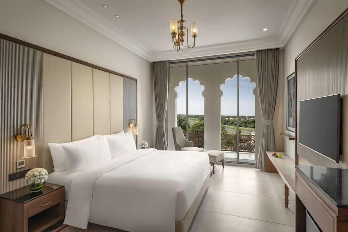 A hotel room with a large bed, a TV, a desk, and a balcony with a view.