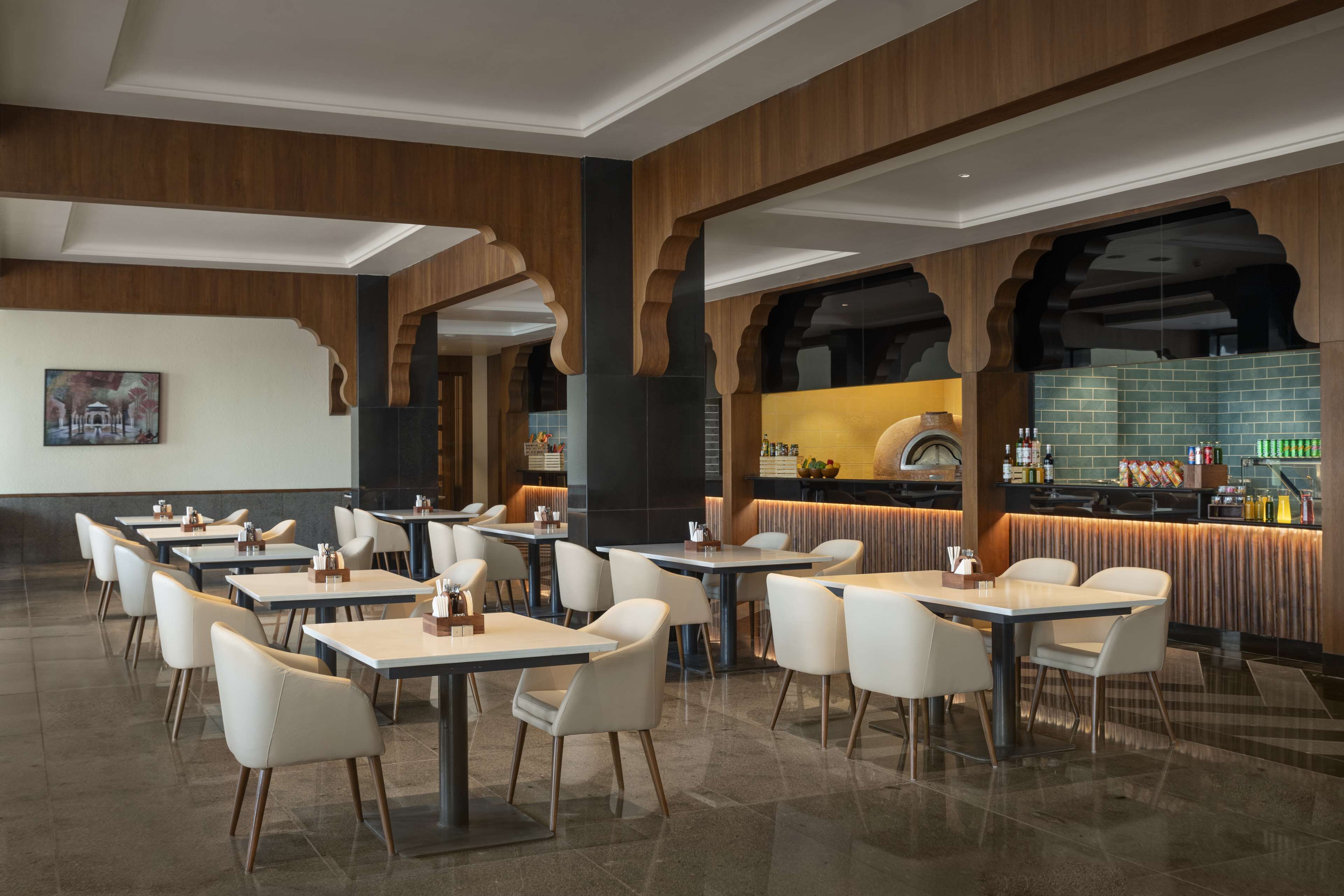 Un restaurant moderne doté de nombreuses tables et chaises, d’un bar et d’une cuisine visible à travers une arche.