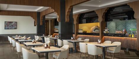 Un restaurant moderne doté de nombreuses tables et chaises, d’un bar et d’une cuisine visible à travers une arche.