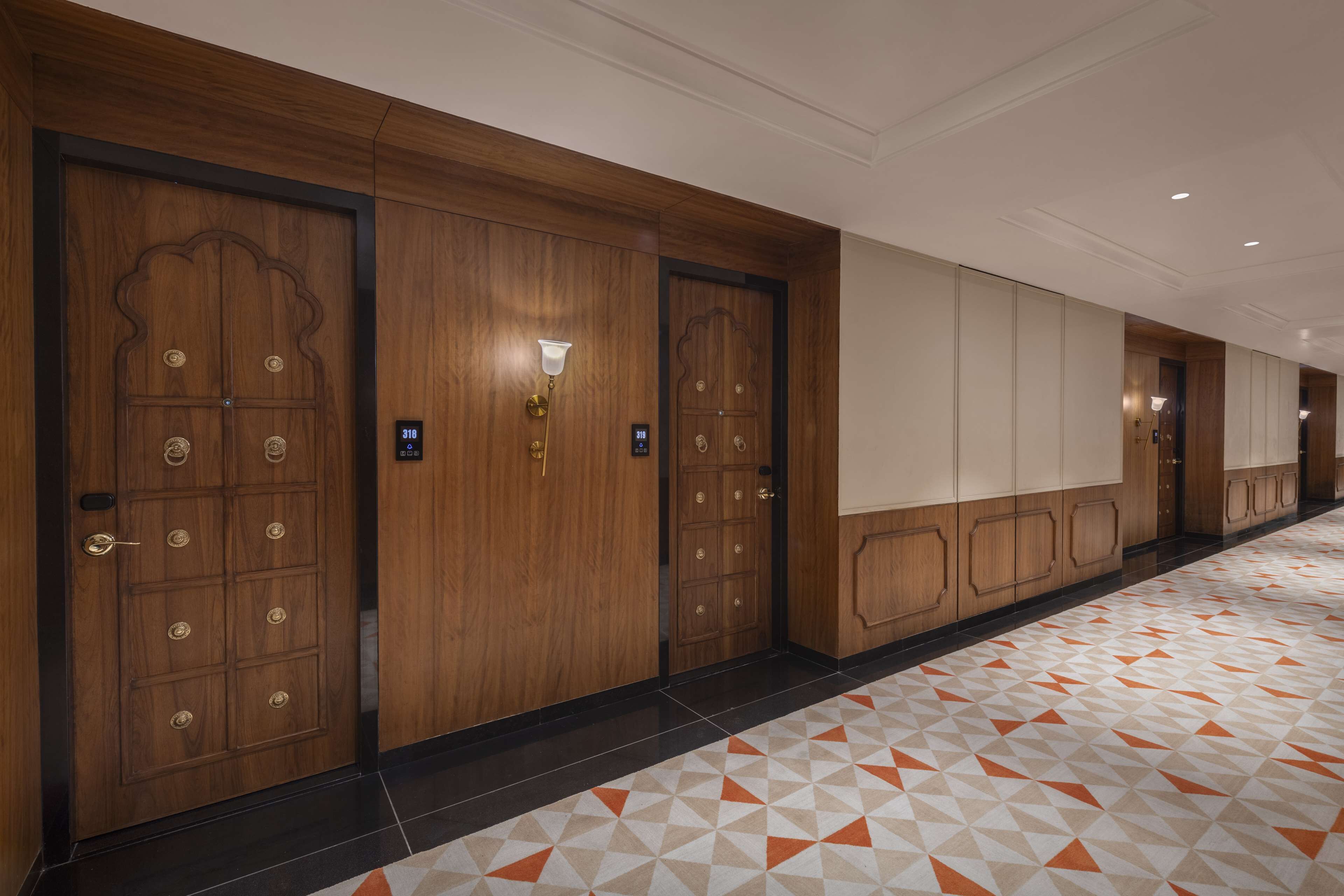 A hotel corridor with wooden doors, a patterned floor, and a light fixture.