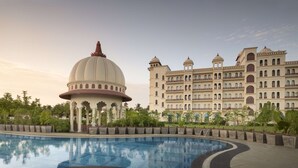 Una piscina grande con una estructura abovedada en primer plano y un edificio de varios pisos con balcones al fondo.