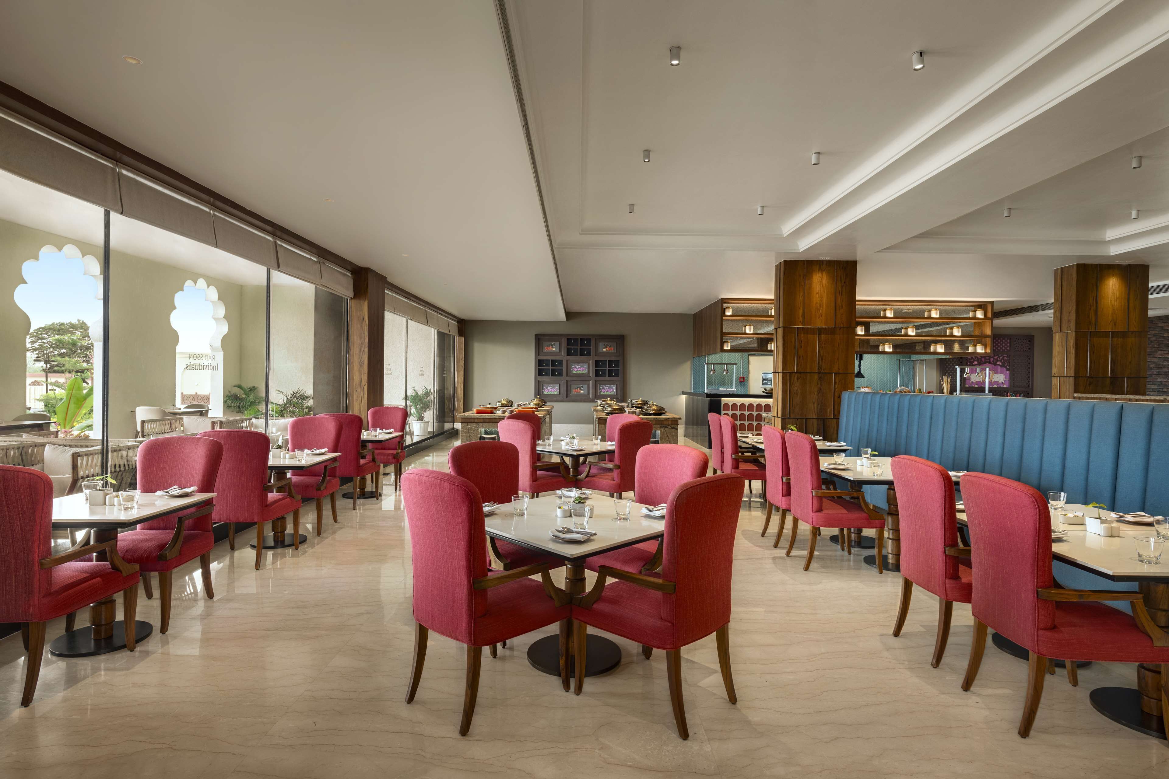 A restaurant with red upholstered chairs and tables, a blue booth area, and a view of the outdoors.
