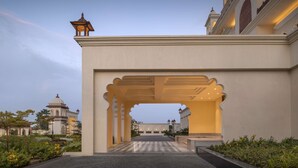 Una imponente entrada con un arco, un jardín cuidado y un edificio tradicional al fondo.