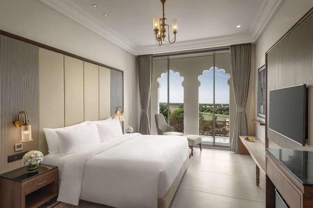 A hotel room with a large bed, a TV, a desk, and a balcony with a view.