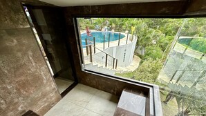 Un bagno moderno con una grande finestra, pavimento in marmo e vista sulla piscina e sul verde circostante.