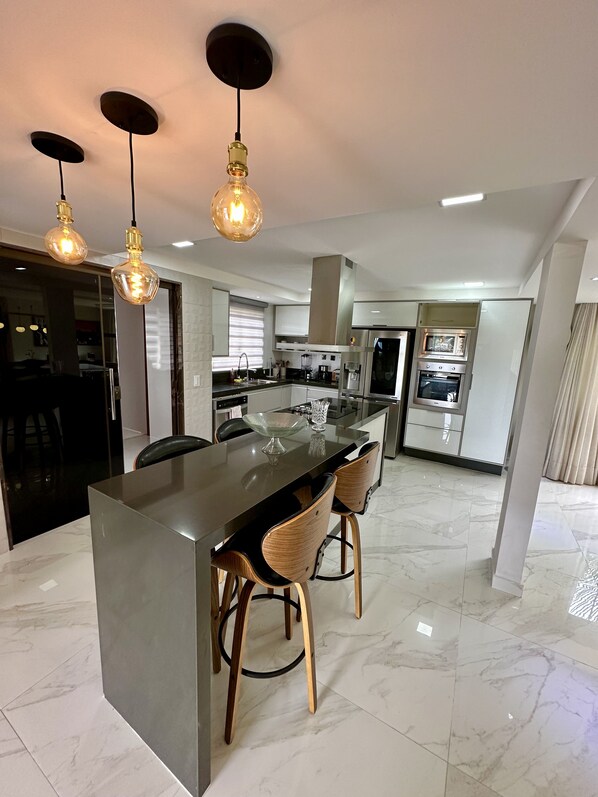 Una cocina moderna con una isla central, electrodomésticos de acero inoxidable e iluminación colgante.