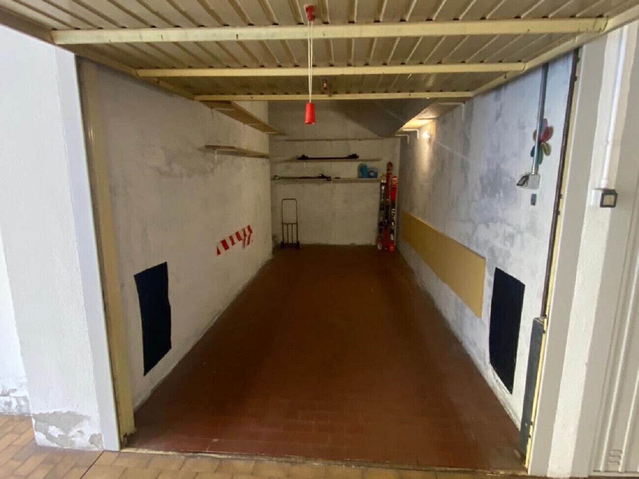 A narrow corridor with a tiled floor, white walls, and a ceiling with exposed beams.