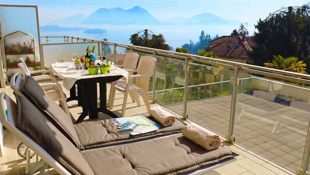 En balkon med bløde siddepladser, et bord med drikkevarer og en menu, samt en smuk udsigt over bjergene.