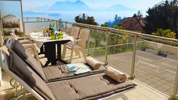 Un balcone con una zona relax imbottita, un tavolo con bevande e un menù, e una vista panoramica sulle montagne.