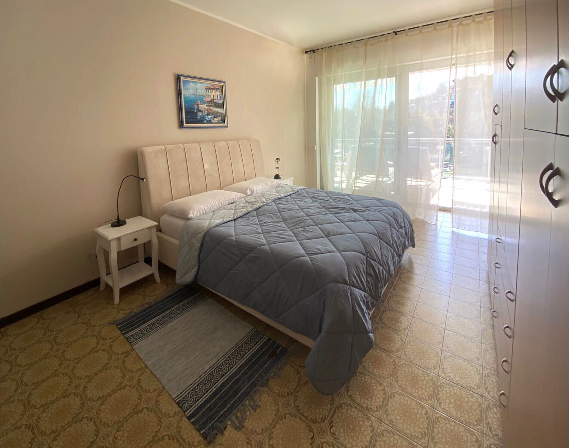 Una camera da letto con un letto, un comodino, una lampada, un tappeto e un quadro appeso al muro.