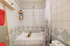 Ein Badezimmer mit Badewanne, Dusche und Toilette. Regale mit Pflegeprodukten und ein Handtuchhalter sind vorhanden.