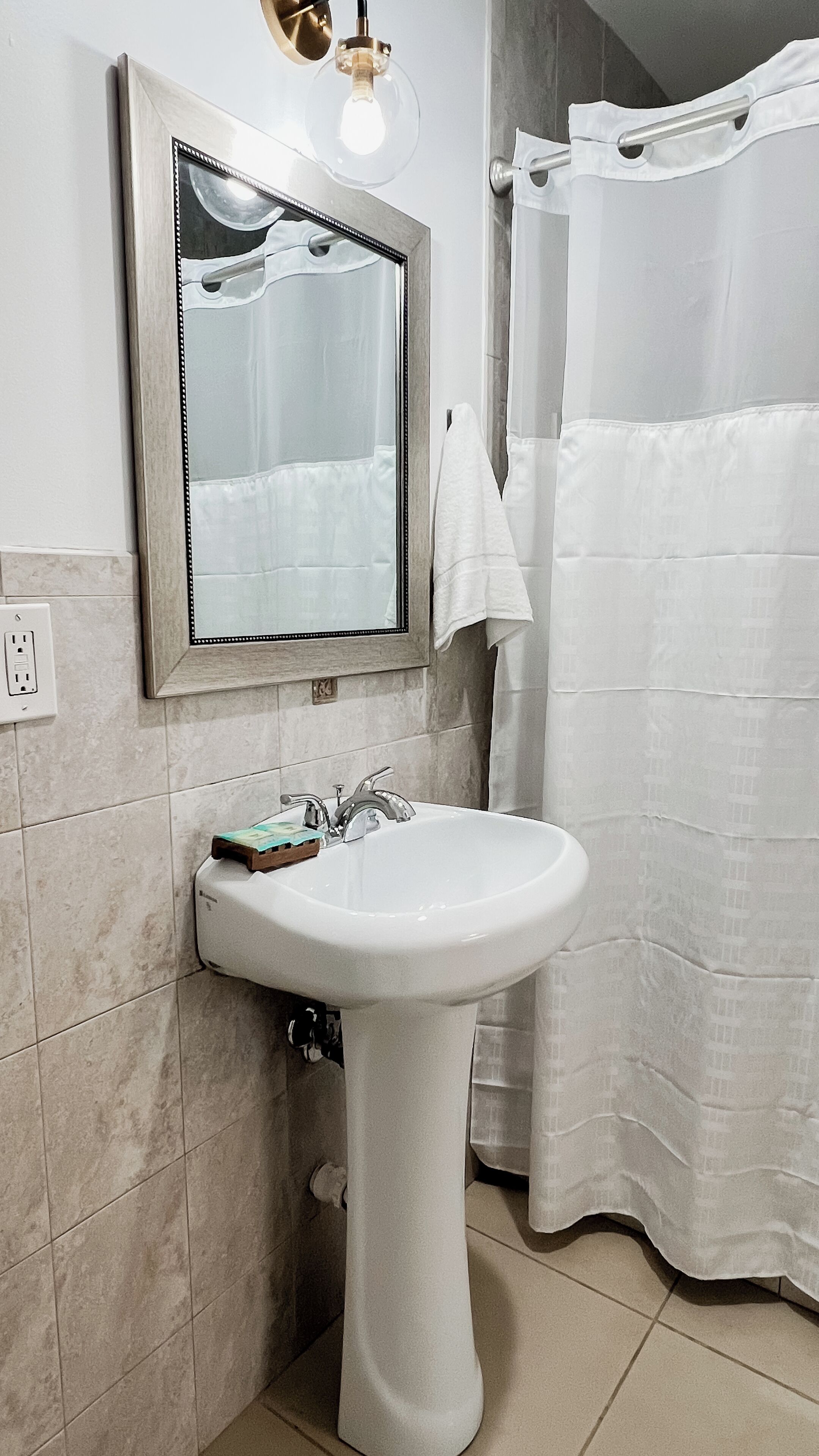 Une salle de bain avec un lavabo sur colonne, un miroir, un porte-serviettes et un rideau de douche.