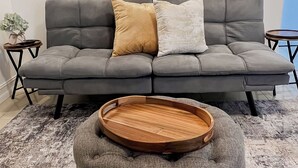 Un canapé gris avec deux coussins, un plateau en bois et une petite table sur laquelle est posée une plante.