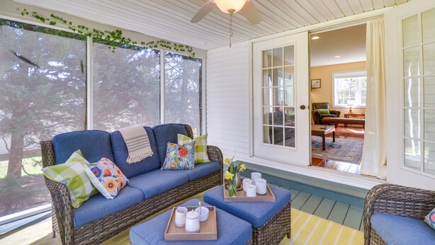 A cozy room with a wicker sofa, blue cushions, and a wooden tray with cups and a vase.