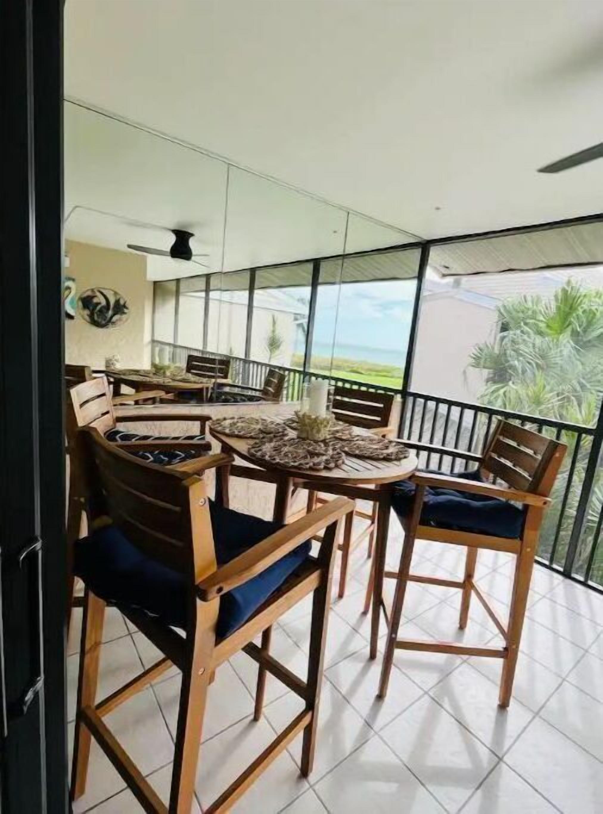 Een balkon met een eettafel en stoelen, grote ramen en uitzicht op de omgeving.