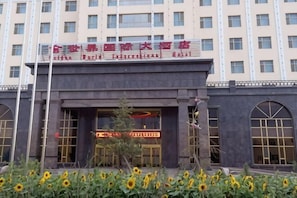 Um edifício com uma entrada imponente, uma placa com caracteres chineses e uma fileira de girassóis na frente.