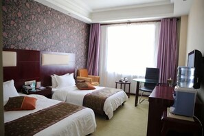 Habitación de hotel con dos camas, un escritorio, una silla, un televisor y una ventana con cortinas.