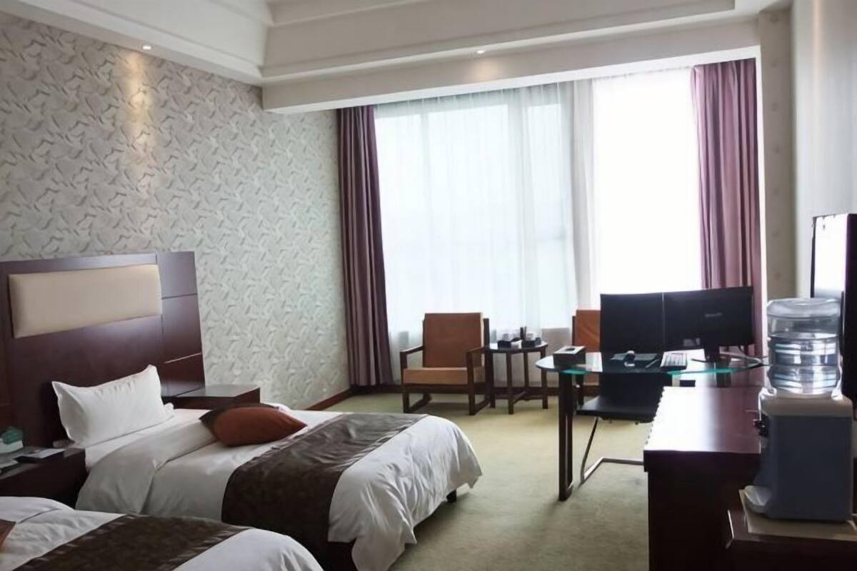 Habitación de hotel con dos camas, un escritorio, una silla, un televisor y un dispensador de agua.